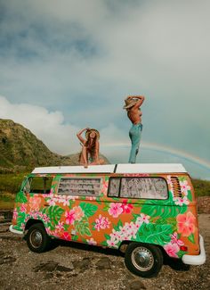 two women standing on top of a van with flowers painted on it and a rainbow in the background