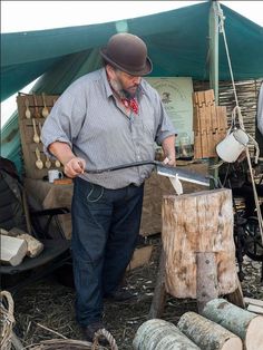 a man with a hat and bow tie chops wood at an outdoor market stall