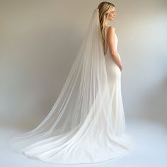 a woman in a wedding dress with a long veil on her head is looking back at the camera