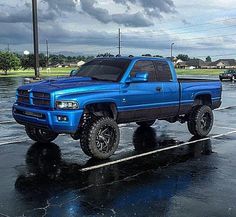 a blue pickup truck parked in a parking lot on a rainy day with dark clouds overhead