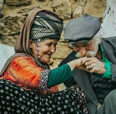 an older man and woman sitting next to each other on the ground smiling at each other