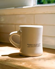 a white coffee cup sitting on top of a wooden counter next to a window sill