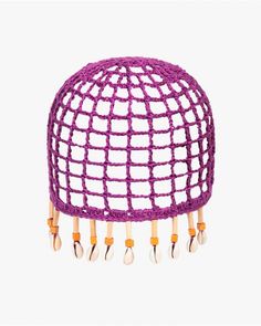 a purple crocheted hat with wooden pins and beads on the top, hanging from a hook