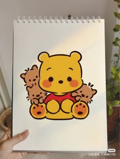 a hand holding up a notebook with a drawing of a teddy bear