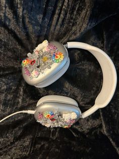 two white headphones sitting on top of a black cloth covered bed with floral decorations