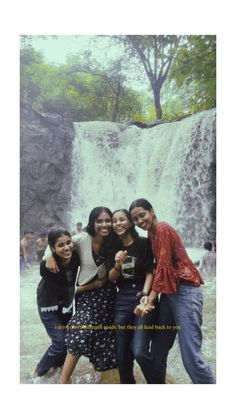 four people posing for a photo in front of a waterfall with water falling down the side