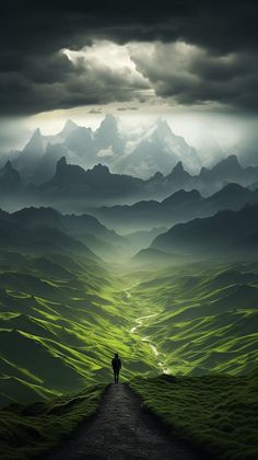 a person walking down a dirt road in the middle of a green valley with mountains