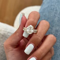 a woman's hand holding a ring with a diamond on it and white nails