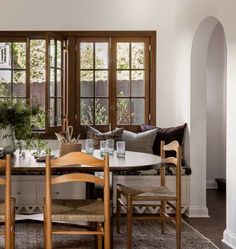 a dining room table with chairs and plants on the table in front of two windows