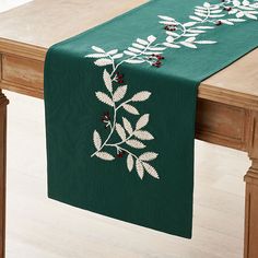 a green table runner with white leaves and berries on it, hanging from a wooden table