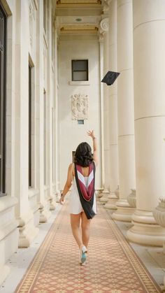 a woman is walking down the hallway with her graduation cap in the air above her head