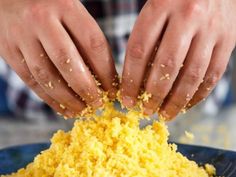 two hands are sprinkling yellow rice into a blue bowl