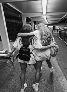 two girls walking down the sidewalk with their arms around each other