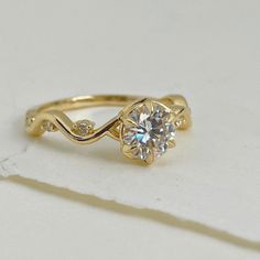 This exquisite engagement ring is a testament to the enduring beauty of the natural world. A radiant Moissanite, cut with precision and set in a classic six-prong setting, takes center stage. Beneath, a delicate leaf motif adds a touch of organic elegance, reminiscent of a forest floor bathed in sunlight. The ring's true magic lies in its flowing band, reminiscent of a gentle stream winding through a verdant landscape. Tiny diamonds, like sparkling dew drops, adorn the band, creating a sense of Ethereal Yellow Gold Ring, Nature-inspired Gold Flower Ring, Nature-inspired Yellow Gold Flower Ring, 14k Gold Art Nouveau Ring, Art Nouveau Yellow Gold Collectible Rings, Radiant Moissanite, Water Lilly, Leaf Motif, Dew Drops