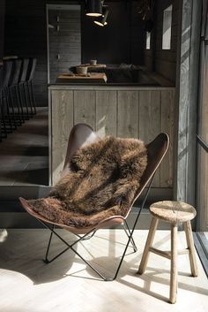 a chair with a fur on it next to a stool in a room filled with chairs