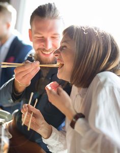 a man and woman eating food with chopsticks