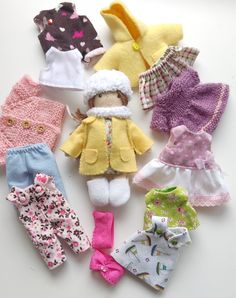 there are many different types of baby clothes on the white surface, including clothing for dolls