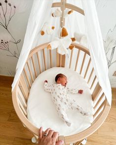 a baby laying in a crib next to a person holding the hand of it's mother