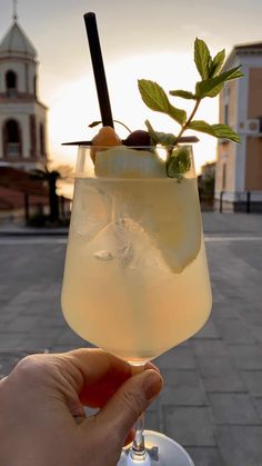 a person holding up a glass filled with ice and lemonade in front of a building