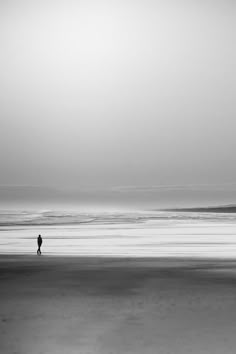 two people are walking on the beach in black and white