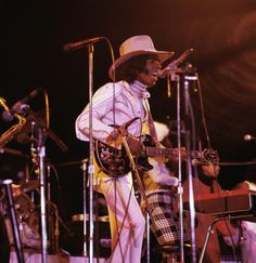 a man with a hat on playing guitar and singing into microphones at a concert