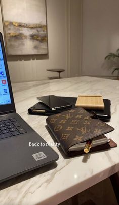 an open laptop computer sitting on top of a white marble table next to a notebook