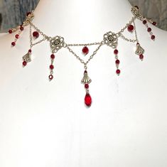 Elegant Victorian gothic style choker necklace of sterling silver chain, antique silver links, and red Swarovski crystals.  Center long dangle is about 2 1/2 inches long.  The necklace is 13 1/2 inches long, fastens with a sterling silver fish hook clasp, and comes nestled comfortably on a bed of cotton in a white cardboard jewelry box.  NA-588-C25 Silver Vampire Style Choker Necklace, Gothic Red Jewelry With Lobster Clasp, Red Gothic Jewelry With Lobster Clasp, Gothic Red Jewelry With Chain, Red Gothic Jewelry With Chain, Gothic Red Chain Jewelry, Victorian Gothic Style, Cardboard Jewelry, Edgy Jewelry