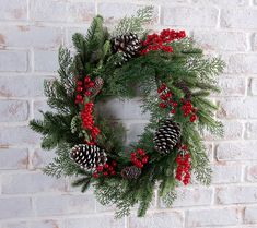 a christmas wreath on a brick wall with pine cones and berries