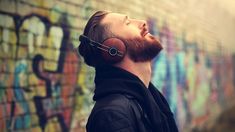 a man wearing headphones standing in front of a wall with graffiti