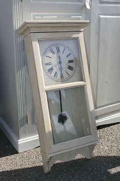 an old clock sitting on the ground in front of a wall with white paint and wood trim