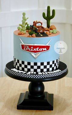 a cake with cars on it sitting on top of a table next to a cactus