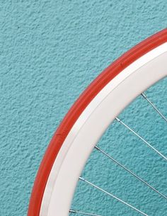 an orange and white bicycle tire against a blue wall with red spokes on it