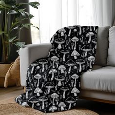 a black and white mushroom print blanket sitting on top of a couch next to a potted plant