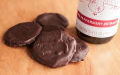 chocolate covered cookies sitting on top of a wooden table next to a bottle of peppermint extract