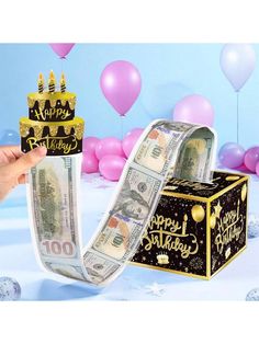 a hand holding a roll of money with a birthday hat on it and balloons in the background