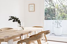 a wooden table with four chairs and a vase on top of it in front of a window