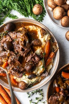 a bowl of stew with carrots, potatoes and parsley next to it on a white surface