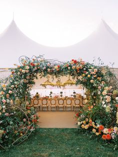 an outdoor ceremony with flowers and greenery on the side, surrounded by white tents