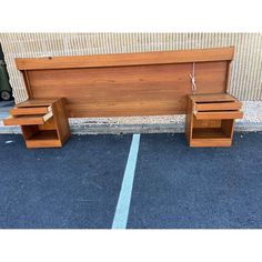 a wooden bench sitting on top of a parking lot next to a wall with two drawers