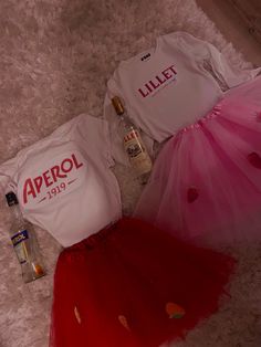 two t - shirts and a tutu skirt are laying on the floor next to an empty bottle