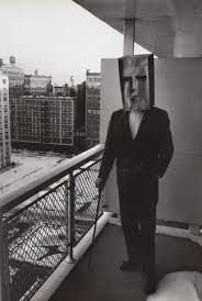 a man in a suit and tie standing on a balcony with buildings in the background