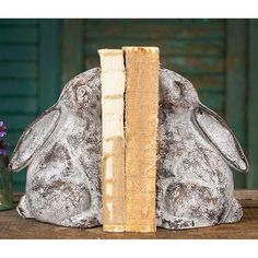 a rabbit statue sitting next to a book on top of a wooden table with purple flowers in the background