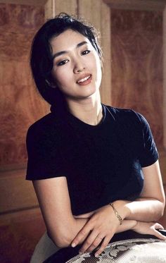 a woman sitting on top of a white chair next to a wooden wall and wearing a black shirt