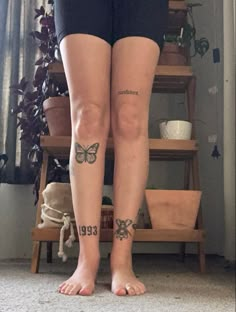 a woman with tattoos on her legs standing in front of a shelf full of plants