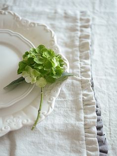 a white plate topped with a green flower on top of a table covered in ruffled linens