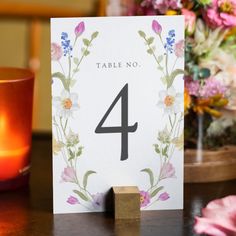 a table number sitting on top of a wooden block next to a candle and flowers