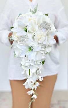 "This beautiful white cascading bouquet is one our our luxurious, high quality bouquets. It is made out real to touch roses, real touch calla lilies, real touch lilies, a spray of silk orchids, silk hydrangeas and a touch of dusty miller. The floral used in this bouquet   feel just like real flowers. This bouquet can also can be arranged with or without shimmering rhinestone brooches. Perfect for your white, minimalistic, or modern wedding!   Dimensions: Measures 10\" across and cascades 23\" long WITH the brooches and 9\" x 23\" WITHOUT the brooches. If you are interested in a bouquet that is a different size or shape for your bridesmaids, please send me a message so that I can accommodate your request.   VISIT MY SHOP  https://www.etsy.com/ca/shop/AdoredOccasions?ref=hdr_shop_menu Check Bride Boutique Flowers, Bridesmaid Floral Bouquet, Wedding Bouquets Real Flowers, Wedding Bouquet Calla Lily, Bride White Bouquet, Long Wedding Bouquets Brides, Hanging Wedding Bouquets, Orchid And Hydrangea Bouquet