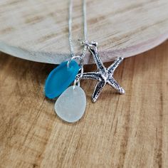 a starfish and sea glass necklace sitting on a wooden table next to a piece of driftwood