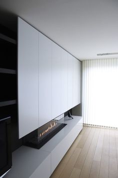 a modern fireplace in the middle of a room with white cabinets and wood flooring