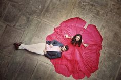 a man and woman laying on the ground with a large red flower in front of them